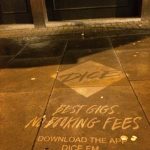 A nighttime photograph of a clean graffiti pavement stencil on a city sidewalk. The stenciled design features the DICE app logo inside a diamond, followed by the text "BEST GIGS. NO BOOKING FEES" in a casual, handwritten-style font, and "DOWNLOAD THE APP DICE.FM" at the bottom.
