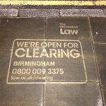 A clean graffiti stencil advertisement on paved ground. A decorative border of stenciled leaves and flowers surrounds text that reads: "#EscapeTheEveryDay with Certified Organic Skincare Shop Sanoflore now at," followed by the official Whole Foods Market logo.