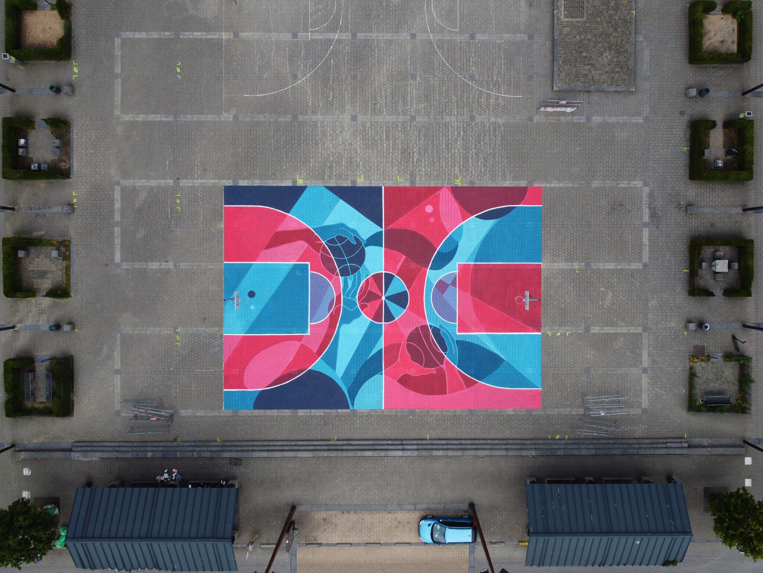 Aerial view of a vibrant, geometric temporary basketball court painted in bright pinks and blues using eco-friendly temporary paint in a public square in Belgium.