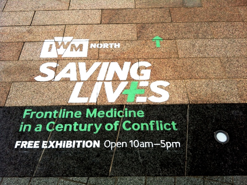 White and green temporary eco-paint stencil on stone paving at MediaCityUK in Salford, providing wayfinding for the IWM North Saving Lives exhibition.